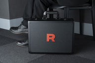 De Team Rocket-attachékoffer uit The Glory of Team Rocket in gebruik, staand op de vloer naast een stoel (officiële sfeerfoto Pokémon Card Game)